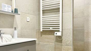 Un baño moderno con un toallero blanco, un cesto de basura redondo y un espejo pequeño y circular.