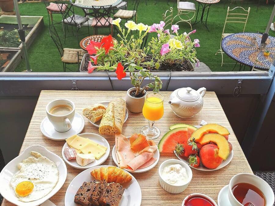 Een balkon met een ontbijtbuffet, inclusief eieren, toast, gebak en fruit, met uitzicht op een tuin met tafels en stoelen.