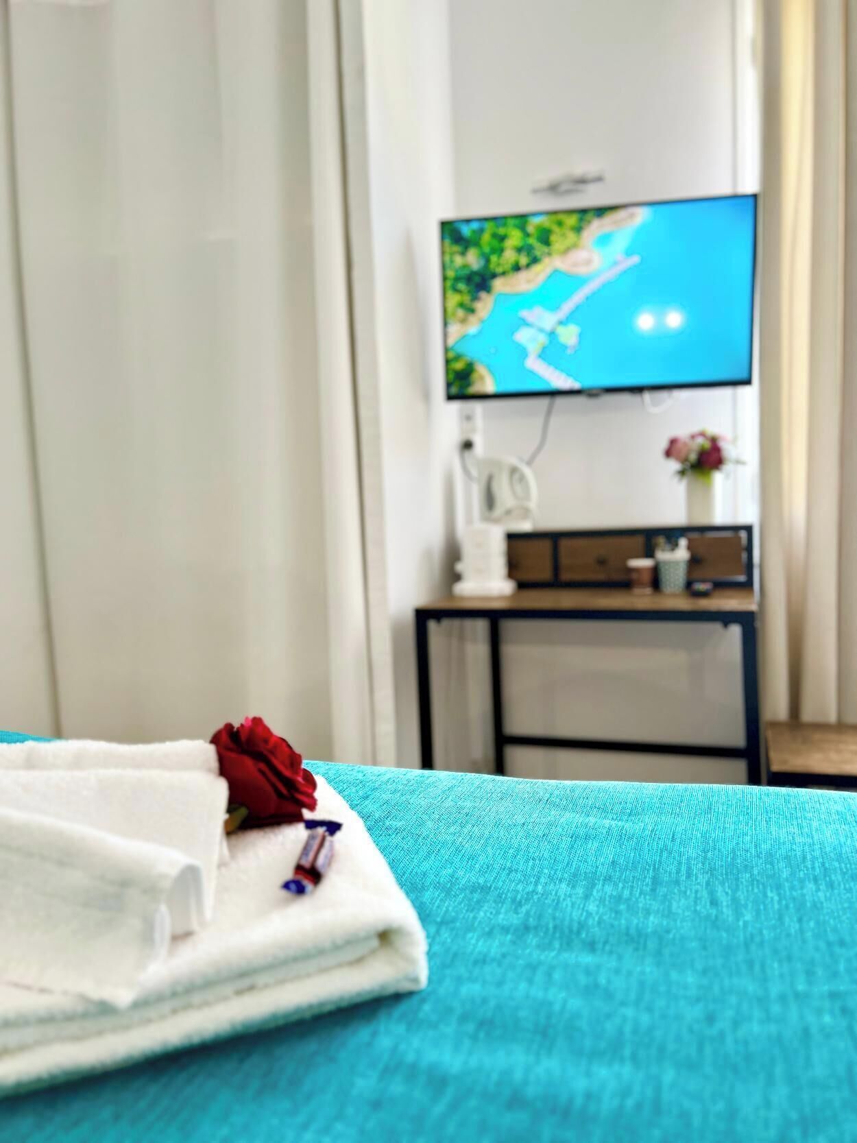 A hotel room with a bed, a TV mounted on the wall, a desk with a chair, and a vase with flowers.