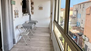 Un balcón con vista a edificios, una mesa con sillas y letreros decorativos en la pared.