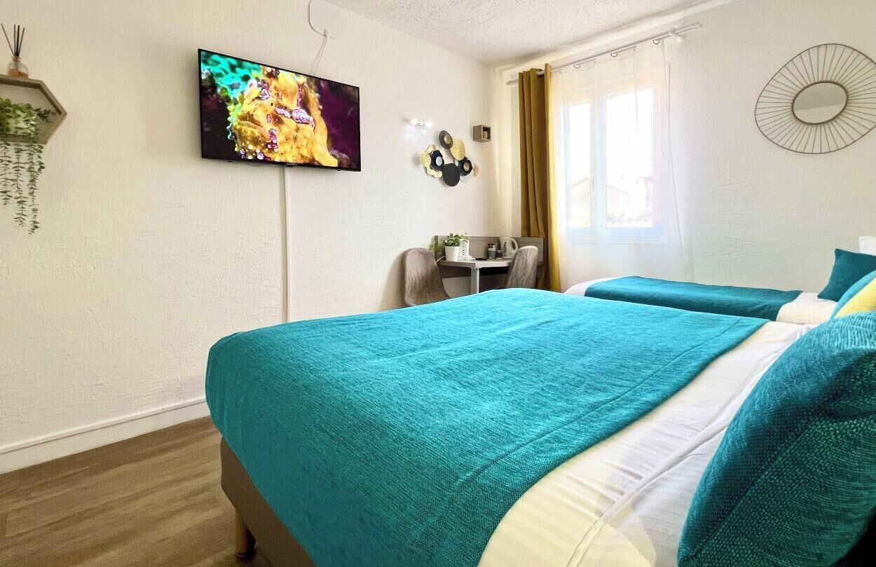 A hotel room with two beds, a TV, a desk, and a window with curtains.