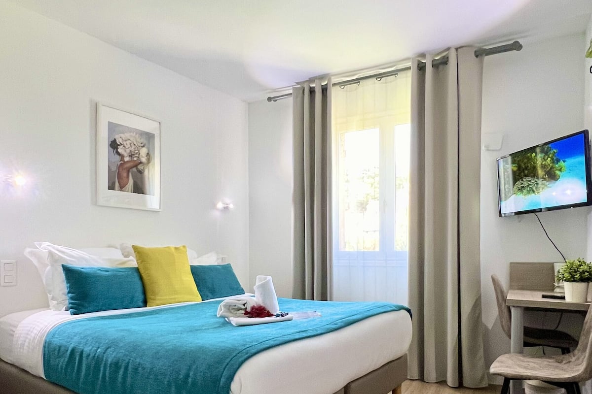 A modern hotel room with a bed, a desk, a chair, a television, and a window with curtains.