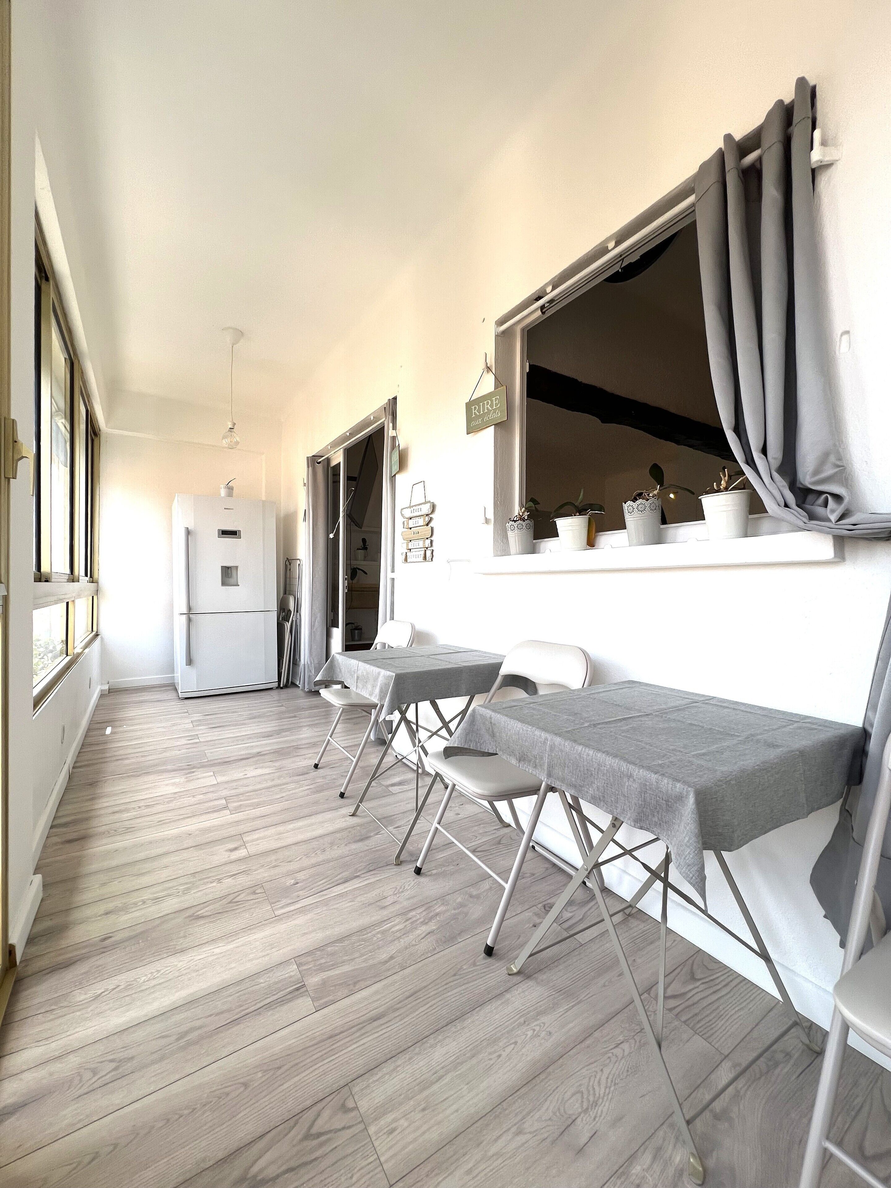 Una habitación con comedor que incluye una mesa larga y sillas, un refrigerador y una ventana con cortinas.