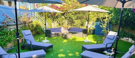 A patio area with outdoor furniture, including lounge chairs and a sofa, under large umbrellas.