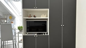 Una cocina moderna con televisor integrado, armarios grises y un comedor con una silla blanca.