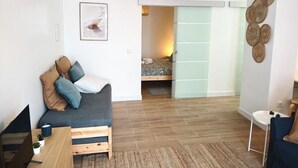 A modern living room with a sofa, a dining table, and a bed in the background. - SandyBeachApartment3 (Porto Santo)