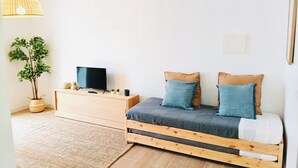 A bedroom with a bed, a TV on a wooden dresser, a potted plant, and a hanging light fixture. - SandyBeachApartment3 (Porto Santo)