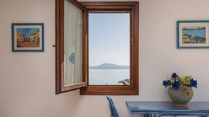 Una habitación con vista al mar, una ventana con marco de madera, una silla, una mesa y dos cuadros en la pared.