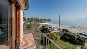 Un balcón con vista a una playa, coches aparcados y cielo despejado.