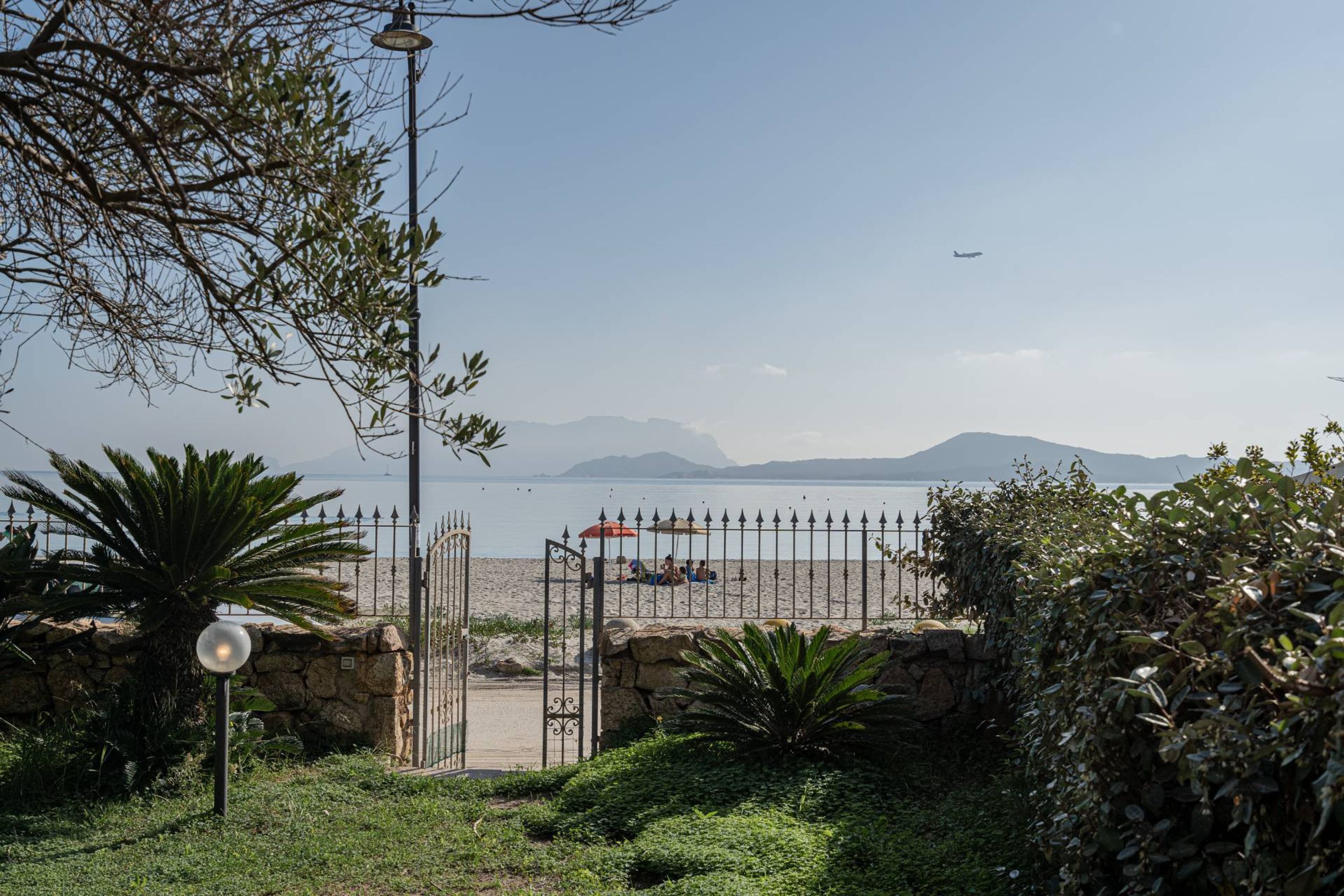 A beach view with a gate, a lamp post, and a stone wall.