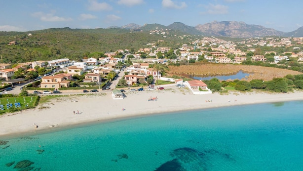 Vista aérea de un pueblo costero con playa, aguas turquesas cristalinas y edificios residenciales.