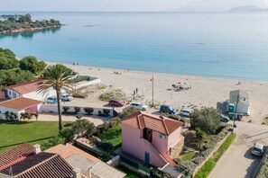 Une propriété située sur la côte, avec vue sur la plage, un petit bâtiment rose et une route bordée de voitures garées.