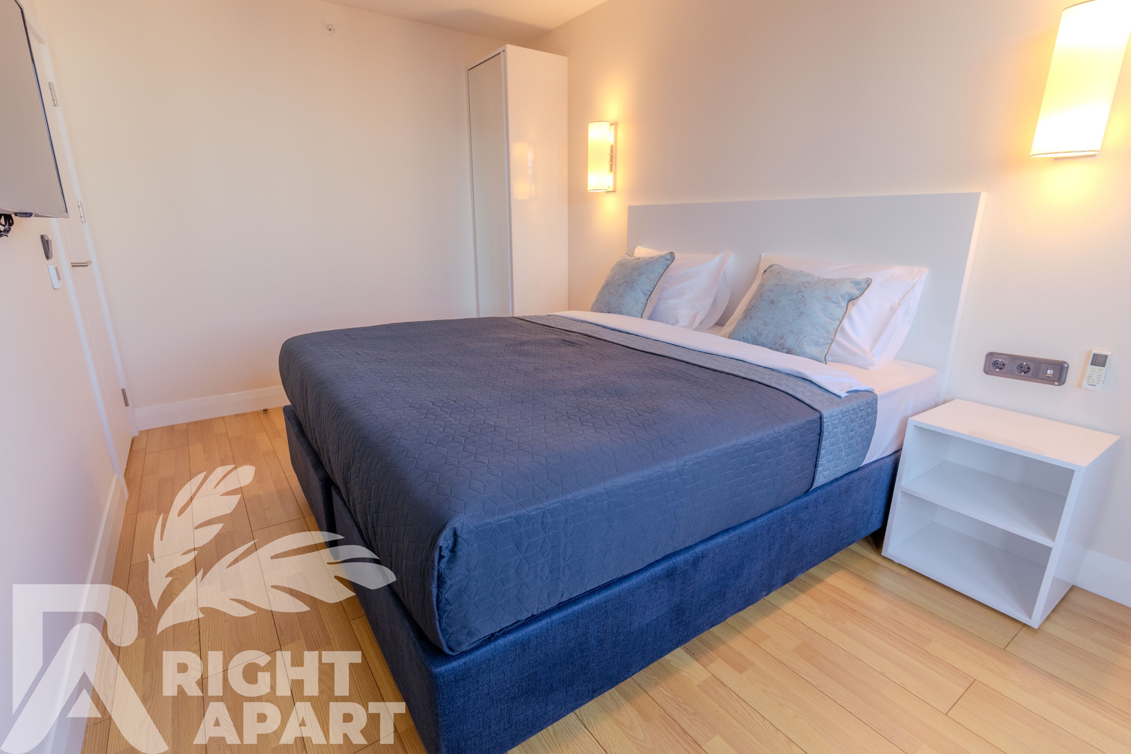 A modern bedroom with a large bed, a nightstand, and a wardrobe.