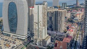 A modern hotel with a distinctive curved facade and a large central window, surrounded by high-rise buildings and a busy urban street. - ORBI CITY RightApart Hotel (Batumi)