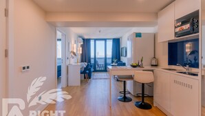 A modern kitchen with white cabinets, a dining area with a table and chairs, and a view of the city through large windows. - ORBI CITY RightApart Hotel (Batumi)