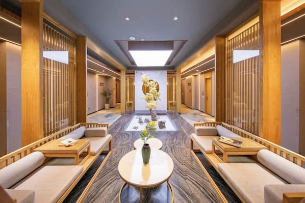 A hotel lobby with a central seating area, a reception desk, and a decorative plant.