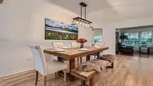 Un comedor con mesa de madera, sillas blancas, un banco y una lámpara colgante.