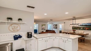 Una cocina moderna con armarios blancos, una isla central y un comedor con mesa y sillas de madera.