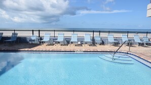 A pool area with lounge chairs and a view of the ocean.