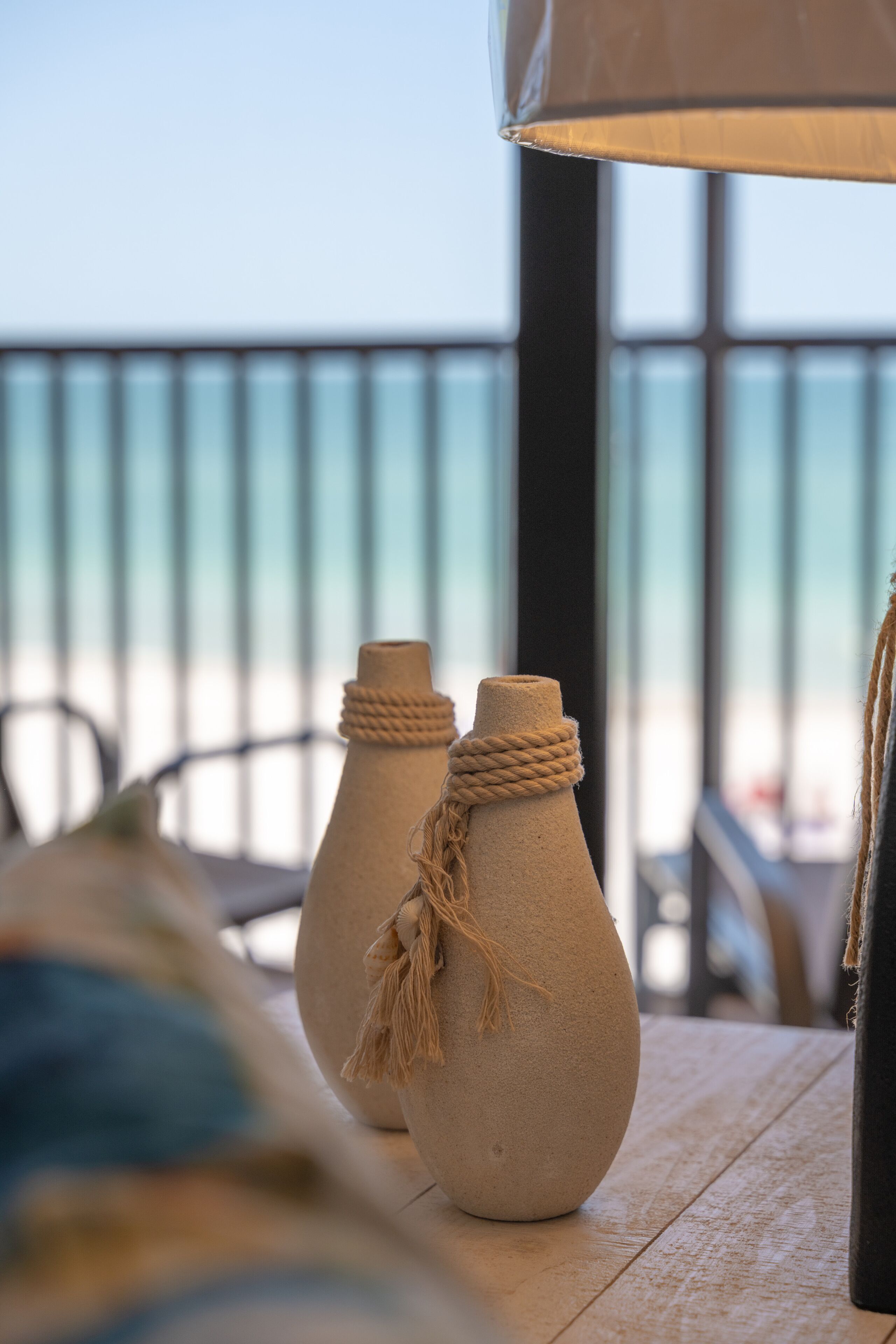 Two ceramic vases with rope decorations on a wooden table, overlooking a balcony with a railing.