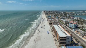 An aerial view of a beach with buildings along the shore, a clear sky, and the ocean.