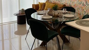 Un comedor moderno con una mesa redonda de vidrio, sillas verde oscuro y un papel tapiz floral.