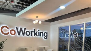 Un espacio de oficina moderno con un letrero que dice 'Coworking', asientos cómodos, una mesa redonda y vistas a un edificio.