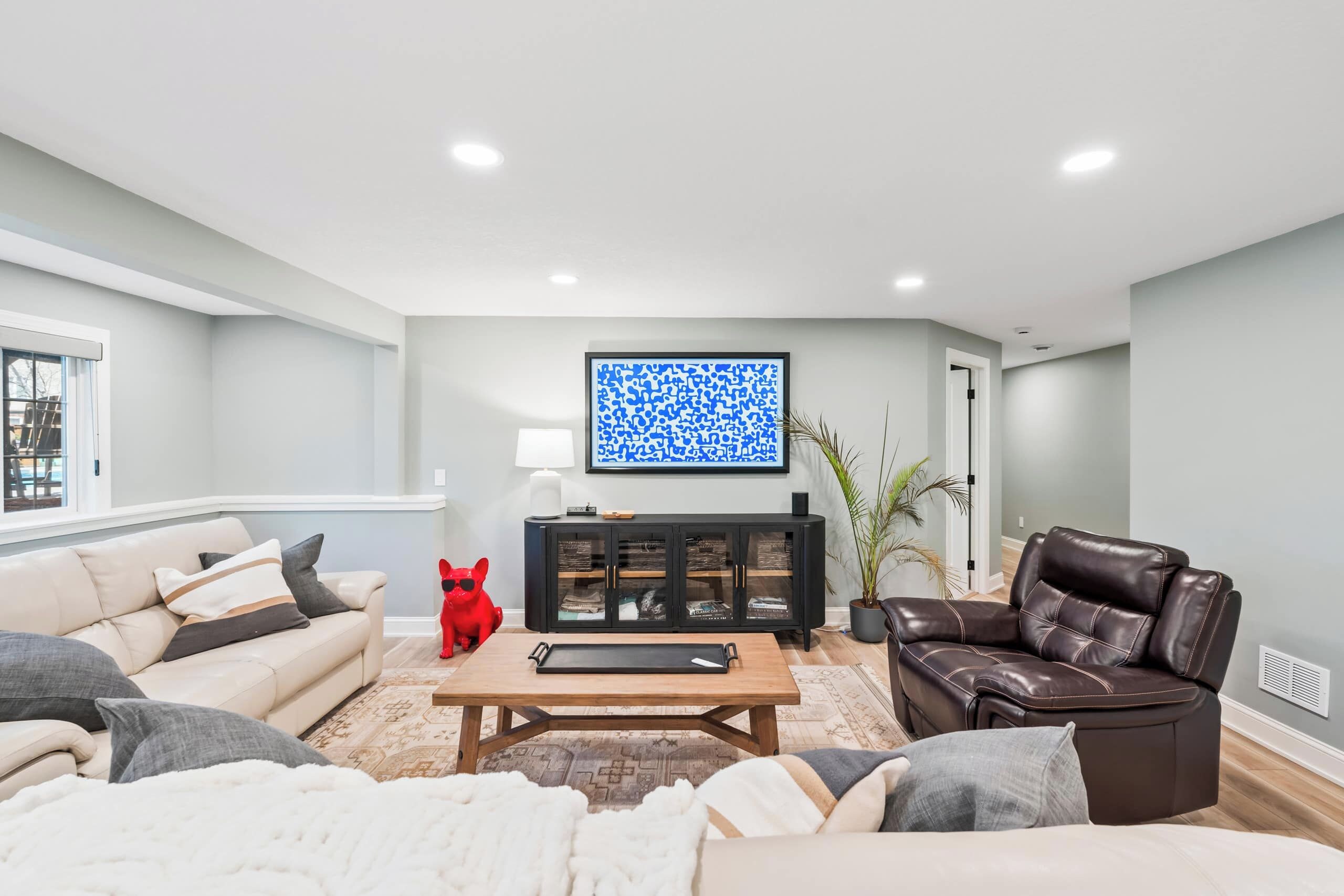 A modern living room with a beige sofa, a brown leather chair, a coffee table, and a black cabinet with glass doors.
