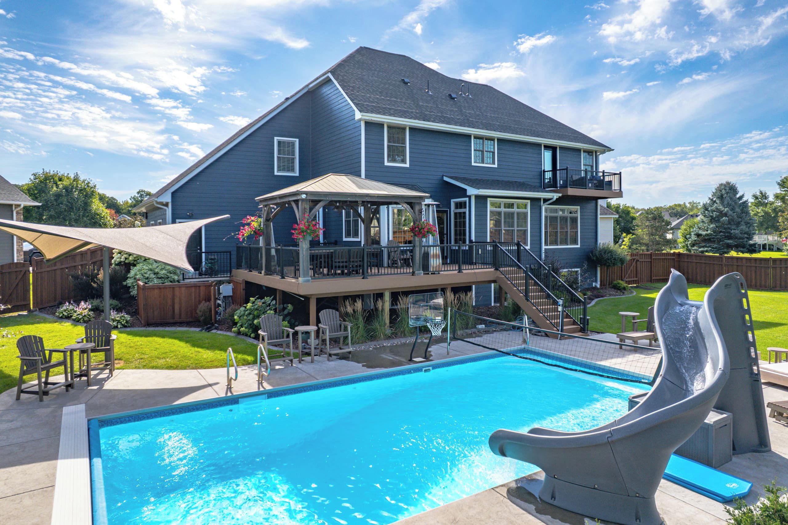 Resort-style backyard in Elk River: the blue two-story home, in-ground pool with a curving water slide and two-level deck.