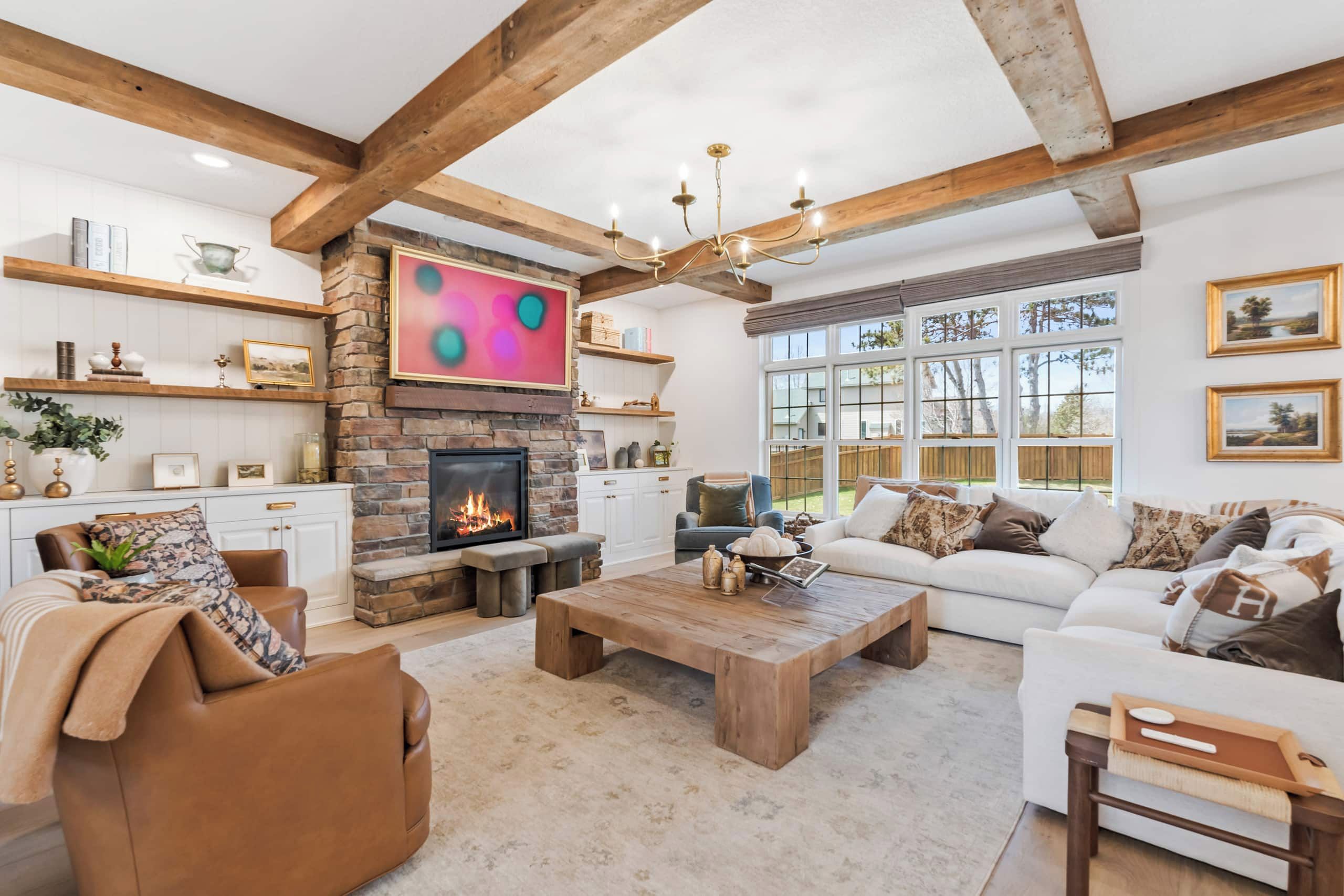 A spacious living room with a fireplace, wooden beams, and a large window.