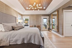 A modern bedroom with a large bed, a chandelier, and a view of the outdoors through a door.
