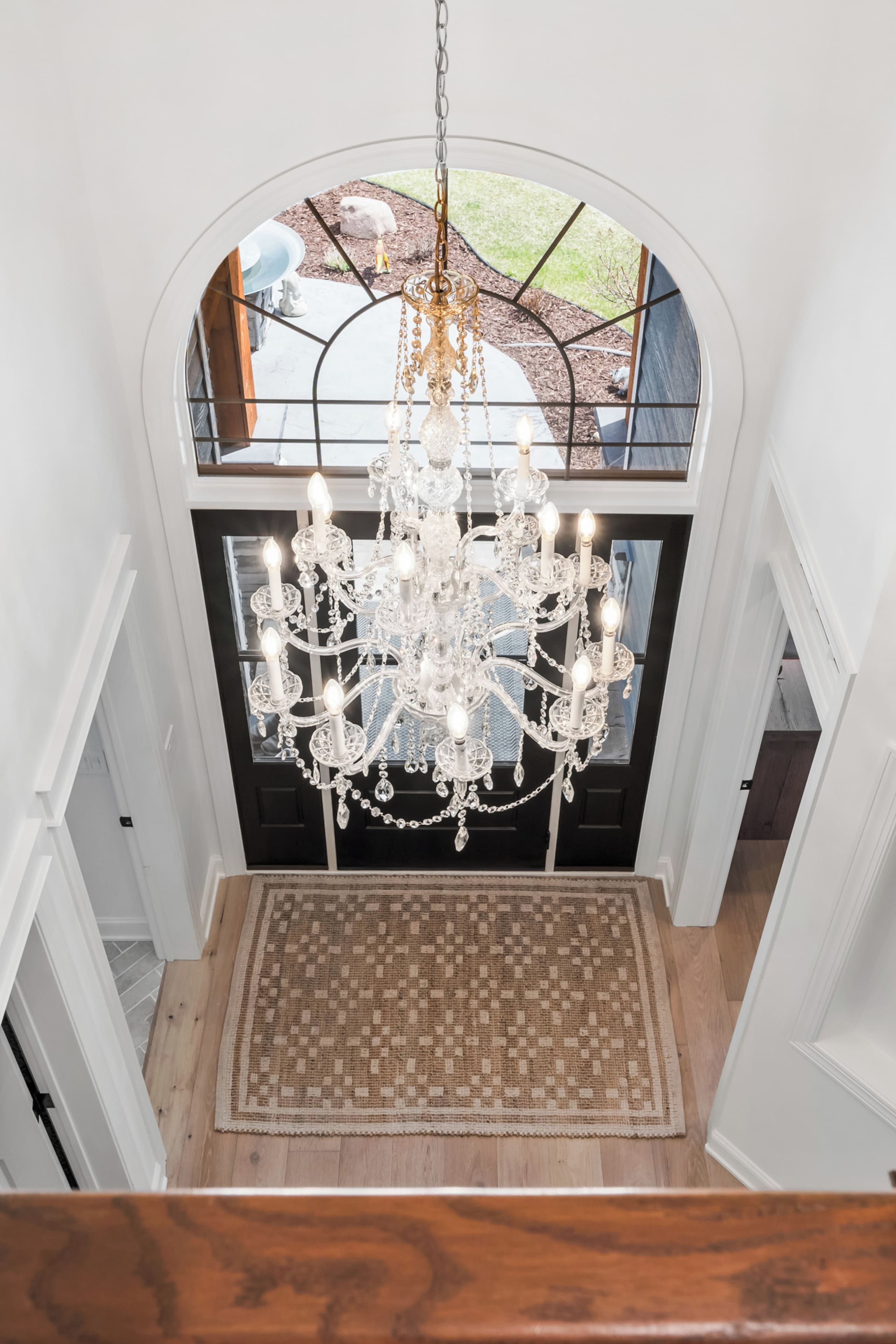 A grand chandelier in a spacious foyer with a high ceiling and a view of the outdoors.