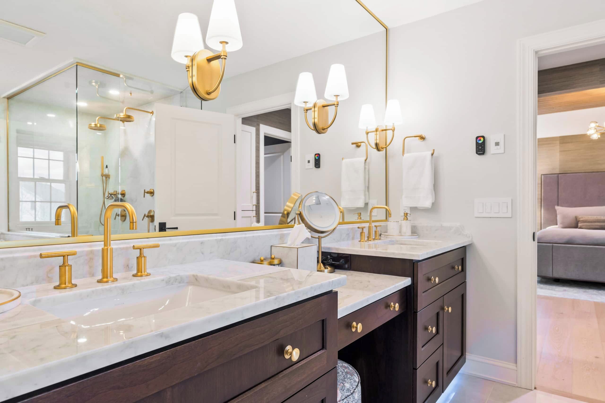 A modern bathroom with dual sinks, gold fixtures, and a large mirror.