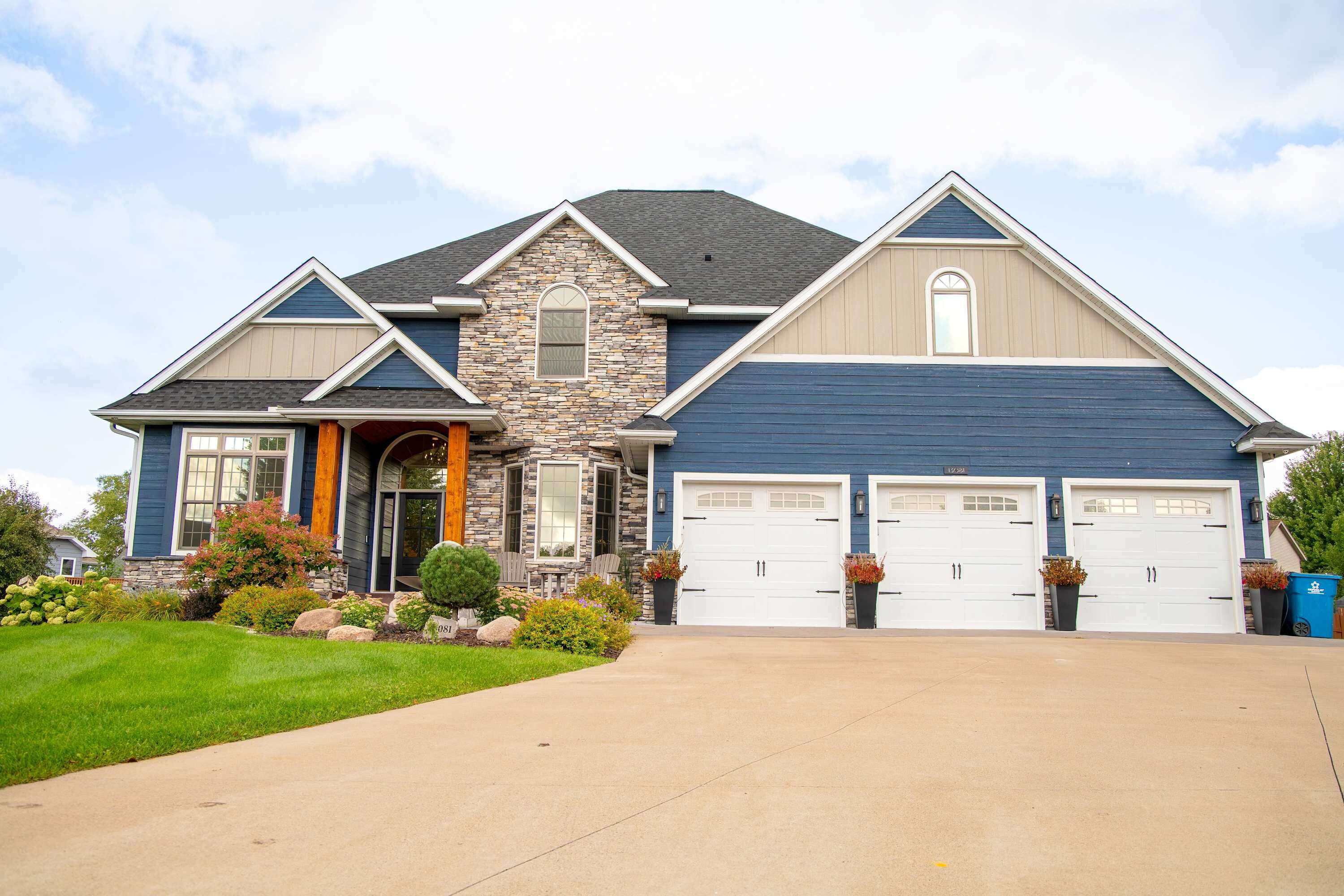 A two-story house with a stone facade, a garage with two doors, and a well-maintained front yard.