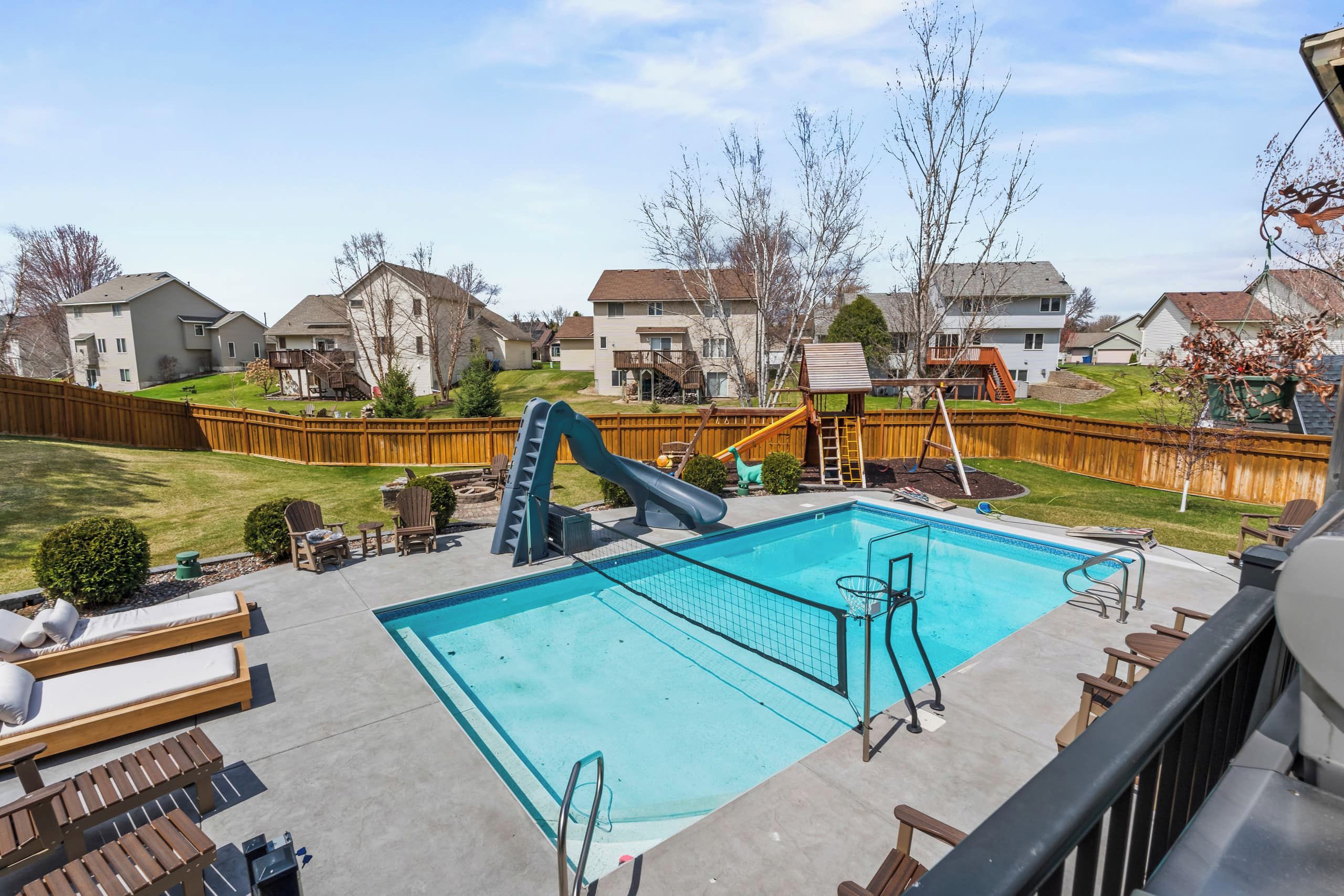 A residential backyard with a swimming pool, a slide, and a wooden deck.