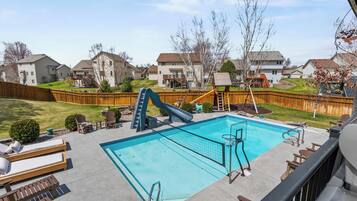 A residential backyard with a swimming pool, a slide, and a wooden deck.