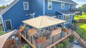 A two-story blue house with a covered deck featuring outdoor furniture and flower pots.