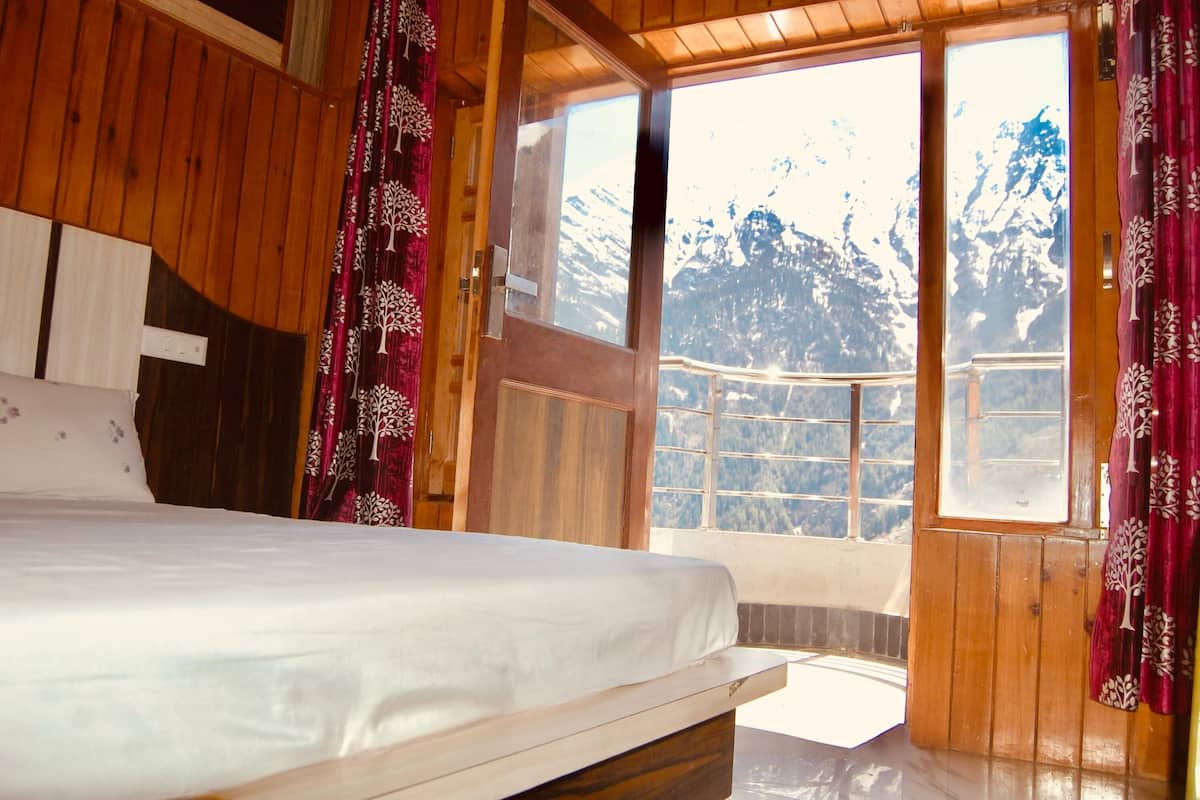 Une pièce en bois avec un lit, une fenêtre donnant sur des montagnes enneigées et des rideaux rouges.