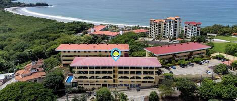 An aerial view of a coastal hotel with multiple buildings, a parking lot, and a beach in the background.
