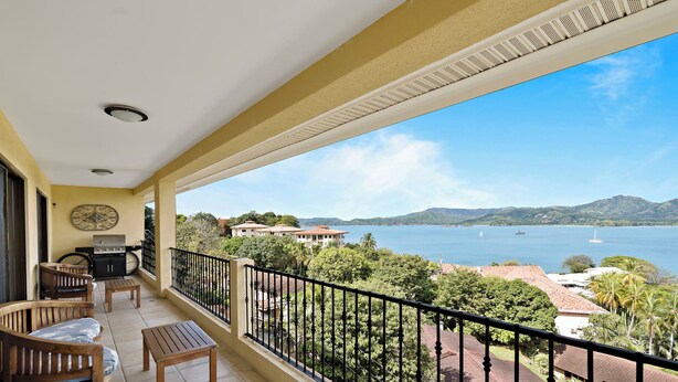 A balcony with a view of the sea, a grill, and a seating area with chairs and a table. - Remodeled Top-Floor Condo with Stunning Wrap-Around Balcony Offering Mountain, Ocean & Marina Views (Cabo Velas)