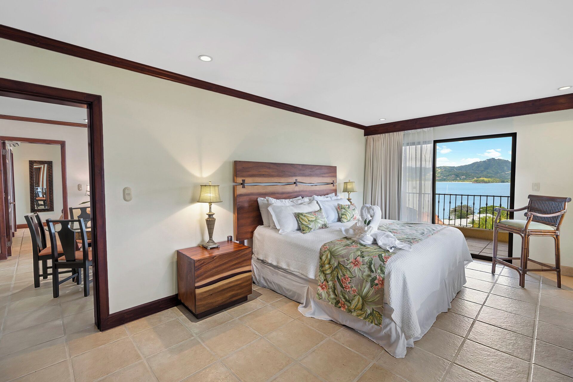 A hotel room with a bed, bedside tables, a chair, and a view of the sea.