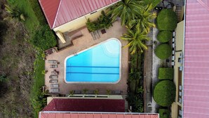 An aerial view of a swimming pool with a red-roofed building, palm trees, and a paved walkway. - Remodeled Top-Floor Condo with Stunning Wrap-Around Balcony Offering Mountain, Ocean & Marina Views (Cabo Velas)