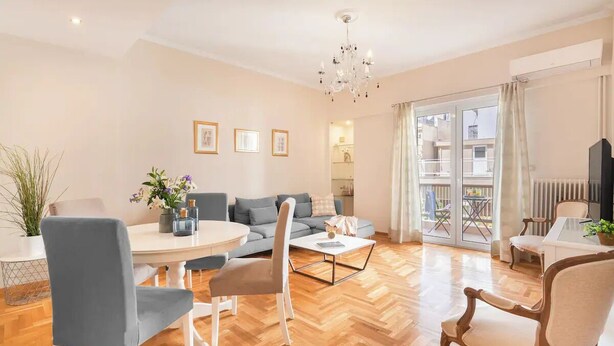 A spacious living room with a wooden herringbone floor, a grey sofa, a white coffee table, and a dining area with a round table and chairs. - Stylish apt steps from Acropolis by GHH (Athens)