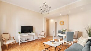 A modern living room with a flat-screen TV, a chandelier, a dining area with a table and chairs, and a sofa. - Stylish apt steps from Acropolis by GHH (Athens)