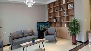 A living room with a sofa, armchair, TV, bookshelf, and a potted plant. - Homeinn Pebble Hotel (Zhengding Airport) (Zhengding)