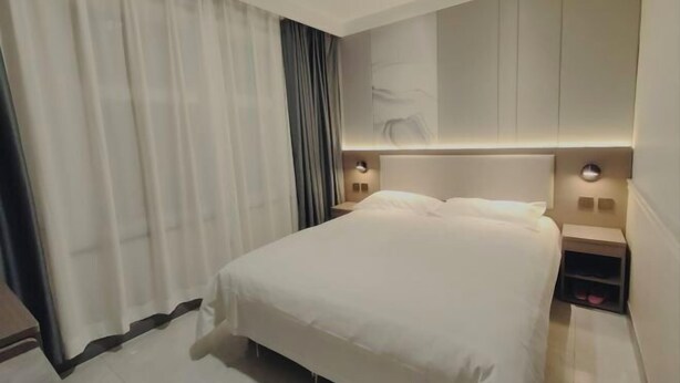 A hotel room with a large bed, a nightstand, a wall-mounted light, and a curtain. - Homeinn Pebble Hotel (Zhengding Airport) (Zhengding)