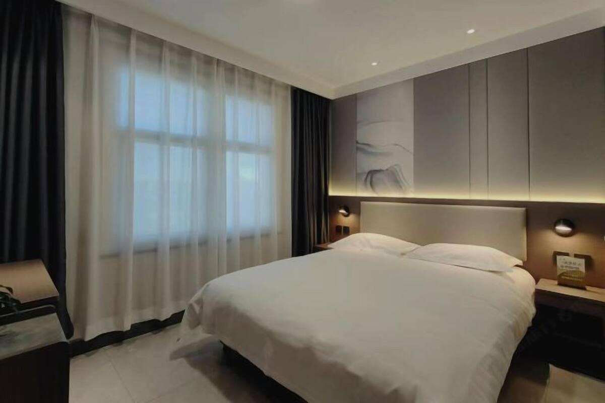 A modern hotel room with a large bed, a nightstand, a lamp, and a wall-mounted light fixture.