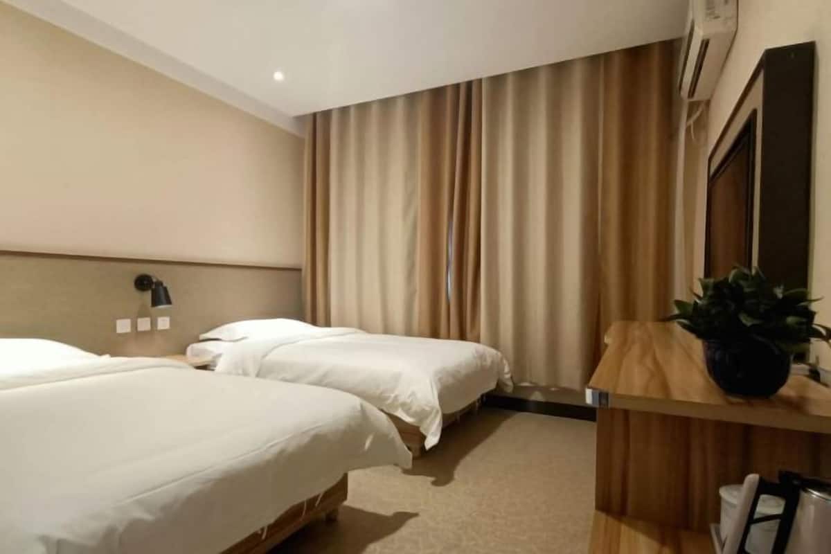 A hotel room with two beds, a wooden desk, a potted plant, and a wall-mounted mirror.