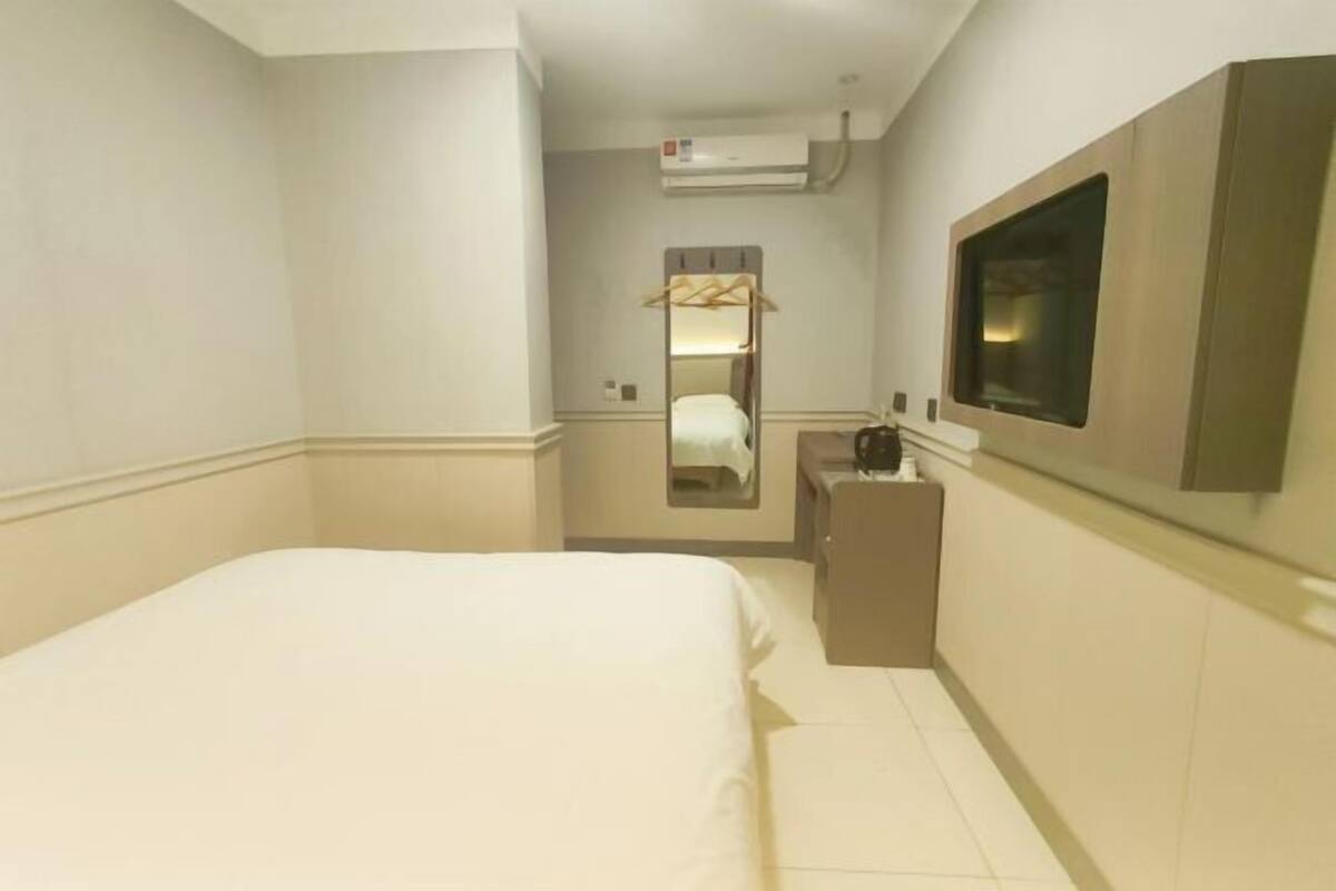 A hotel room with a bed, a mirror, a TV, and a small desk with a lamp.