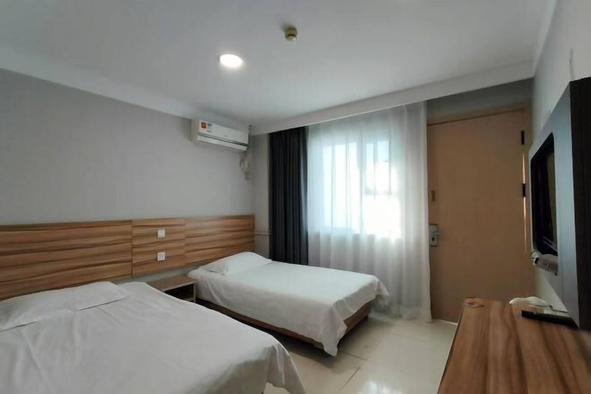 A hotel room with two beds, a wooden headboard, a flat-screen TV, and a window with curtains.